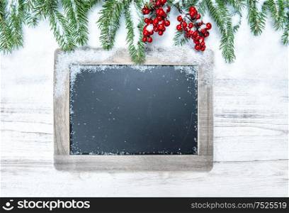 Christmas decoration. Evergreen tree branch with red berries and chalkboard on wooden background. Vintage style toned picture