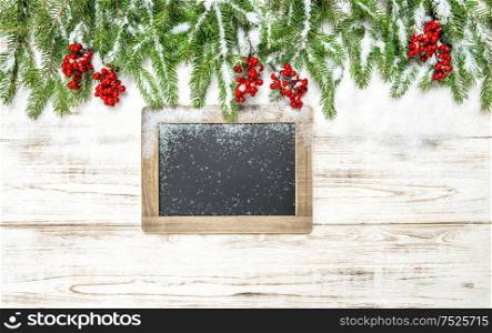 Christmas decoration. Evergreen tree branch with red berries and chalkboard on wooden background