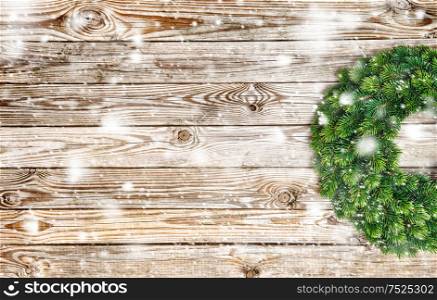Christmas decoration evergreen wreath on rustic wooden texture. Vintage background with falling snow effect