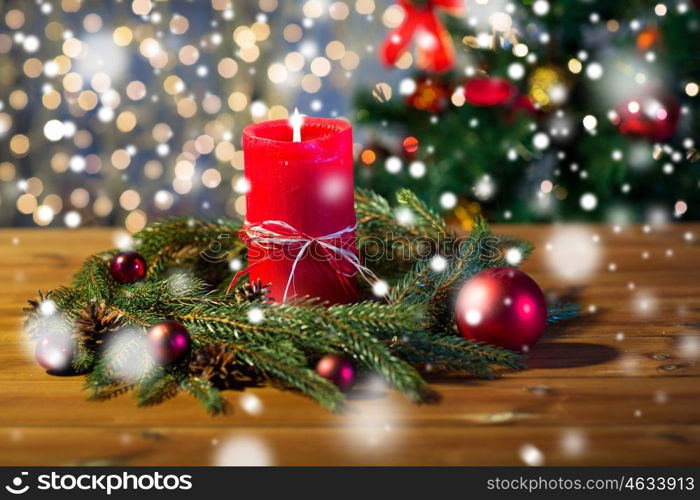 christmas, decoration, holidays and advertisement concept - close up of natural green fir branch wreath with red burning candle on wooden board