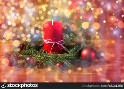 christmas, decoration, holidays and advertisement concept - close up of natural green fir wreath with red burning candle over lights