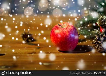 christmas, decoration, holidays and new year concept - close up of red apple with fir branch decoration on wooden table