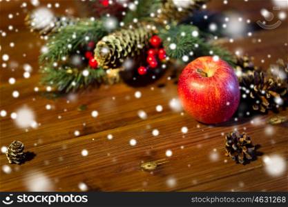 christmas, decoration, holidays and new year concept - close up of red apple with fir branch decoration on wooden table
