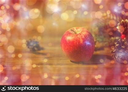 christmas, decoration, holidays and new year concept - close up of red apple with fir branch decoration on wooden table over lights