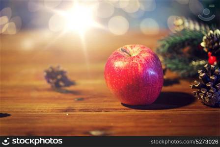 christmas, decoration, holidays and new year concept - close up of red apple with fir branch decoration on wooden table. close up of apple with fir decoration on wood