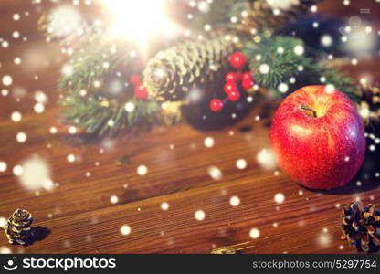 christmas, decoration, holidays and new year concept - close up of red apple with fir branch decoration on wooden table. close up of apple with fir decoration on wood