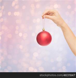 christmas, decoration, holidays and people concept - close up of woman hand holding christmas ball over rose quartz and serenity lights background
