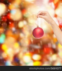 christmas, decoration, holidays and people concept - close up of woman hand holding christmas ball over red lights background