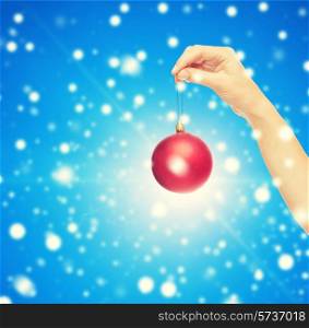 christmas, decoration, holidays and people concept - close up of woman hand holding christmas ball blue snowy background