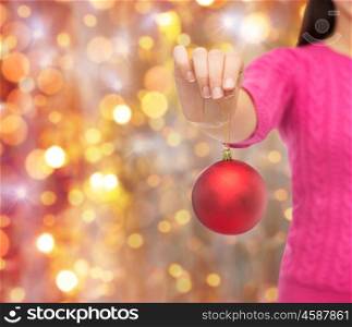 christmas, decoration, holidays and people concept - close up of woman in pink sweater holding christmas ball over lights background
