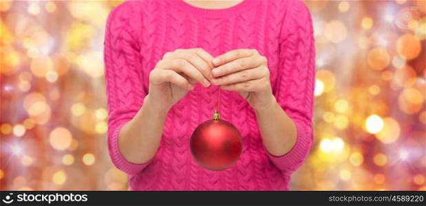 christmas, decoration, holidays and people concept - close up of woman in pink sweater holding christmas ball over lights background