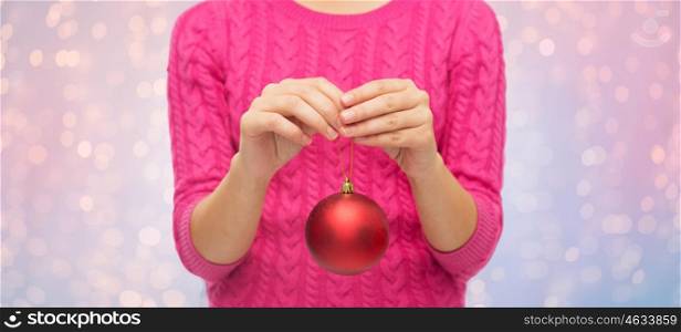 christmas, decoration, holidays and people concept - close up of woman in pink sweater holding christmas ball over rose quartz and serenity lights background