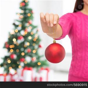 christmas, decoration, holidays and people concept - close up of woman in pink sweater holding christmas ball over living room and tree background