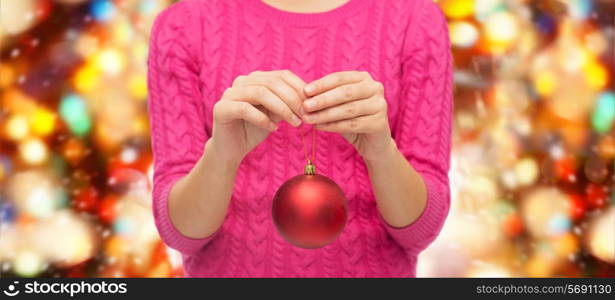 christmas, decoration, holidays and people concept - close up of woman in pink sweater holding christmas ball over red lights background