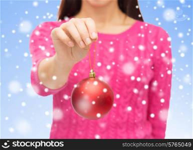 christmas, decoration, holidays and people concept - close up of woman in pink sweater holding red christmas ball over blue background with snow
