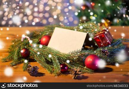 christmas, decoration, holidays, greeting and advertisement concept - close up of natural green fir branch wreath with white blank paper sheet and decorations on wooden board