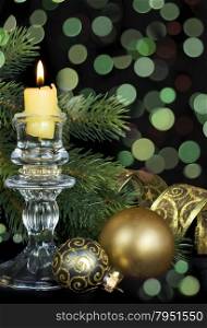 Christmas decoration in green tones with a burning candle, glass balls and beautiful bokeh on a black background