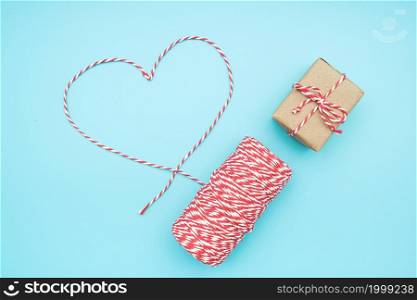Christmas decoration red and white twine in shape of heart and gift box on blue background. Concept christmas gift wrapping . Top view Flat lay Copy space Template for design, postcard, invitation.. Christmas decoration red and white twine in shape of heart and gift box on blue background. Concept christmas gift wrapping . Top view Flat lay Copy space Template for design, postcard, invitation