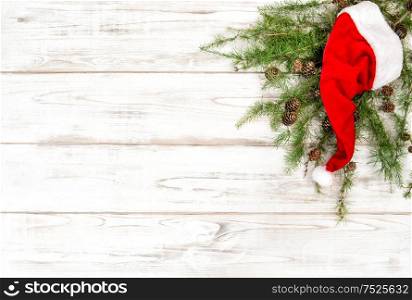 Christmas decoration. Red Santa Claus hat with green pine tree branches on wooden background