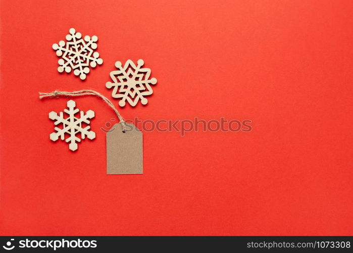 Christmas decoration, three little wooden snowflakes and craft tag on bright red background, copy space. Festive, New Year, sales concept. Horizontal, flat lay. Minimal style. Top view.