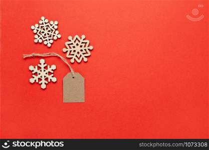 Christmas decoration, three little wooden snowflakes and craft tag on bright red background, copy space. Festive, New Year, sales concept. Horizontal, flat lay. Minimal style. Top view.