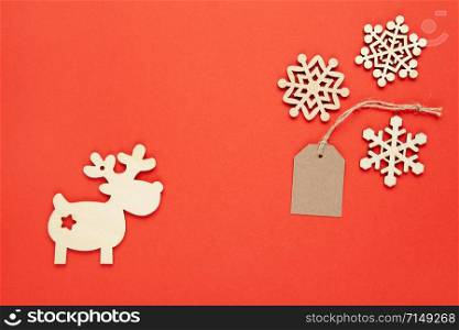 Christmas decoration, three little wooden snowflakes, craft tag, deer on bright red background. Festive, New Year, sales, eco friendly concept. Horizontal, flat lay. Minimal style. Top view.