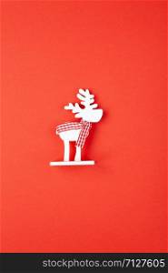 Christmas decoration, toy white deer in checkered scarf on red background. Festive, New Year concept. Vertical, flat lay. Minimal style. Top view.