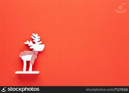 Christmas decoration, toy white deer in checkered scarf on red background with copy space. Festive, New Year concept. Horizontal, flat lay. Minimal style. Top view.