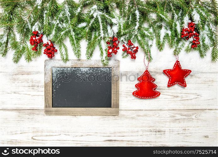 Christmas decoration. Tree branches with red berries, ornaments and chalkboard on wooden background