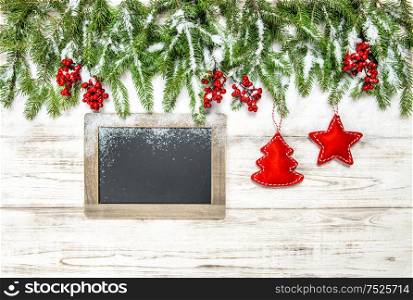 Christmas decoration. Tree branches with red berries, ornaments and chalkboard on wooden background