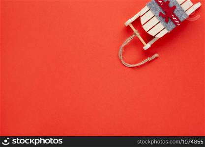 Christmas decoration, tree toy, wooden sled with deer on red background with copy space. Festive, New Year concept. Horizontal, flat lay. Minimal style. Top view.