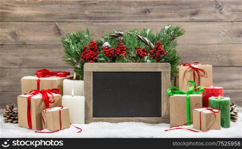 Christmas decoration with burning candles and gift boxes. Christmas tree branches in basket. Chalkboard for your text