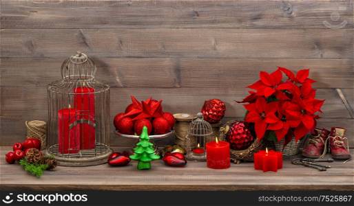 Christmas decoration with burning candles, antique baby shoes, red flower poinsettia, stars and baubles. Retro style toned picture