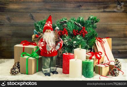 Christmas decoration with Santa Claus, burning candles and gift boxes. Fir tree branches in basket. Vintage style toned picture