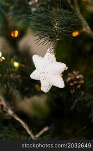 Christmas decorations, a white toy star with sparkles hangs on the tree, warm light. Close-up. Christmas decorations, a white toy star with sparkles hangs on the tree, warm light. Close-up.