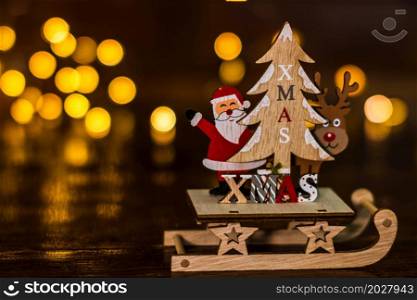 Christmas decorations against blurred background. Close up of a wooden Christmas sledge with Santa Claus, a reindeer and Christmas tree.