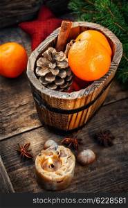 Christmas decorations for the holiday. Wooden bucket with tangerines and pine cone and a burning Christmas candle