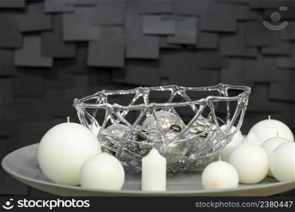 Christmas decorations of ball shaped candles and vases with Christmas toys on a white plate on a dark background with tiles. white candles decorated on a plate