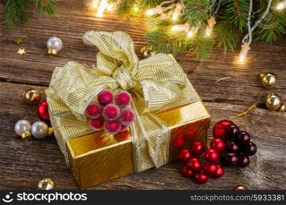christmas decorations with gift box. golden christmas gift box with lights on evergreen tree in background on wooden table