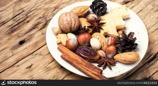 Christmas decorations with nuts, spices and bumps on a plate. Christmas plate with nuts, spices and cedar cone