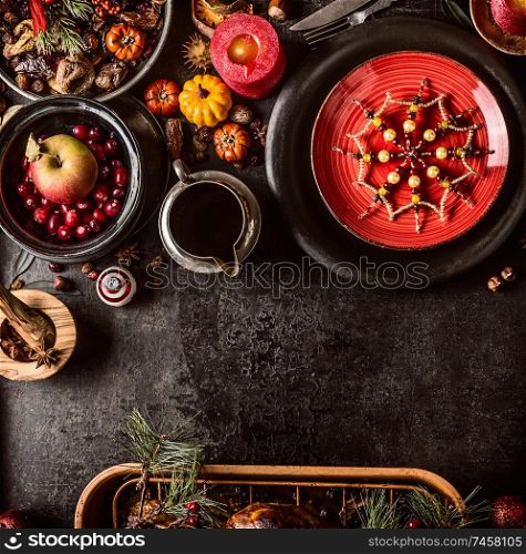 Christmas dinner background with festive table setting, snowflakes decoration, sauce, fresh cranberries and apple, pumpkins, nuts and pine branches. Dark rustic style. Top view. Copy space