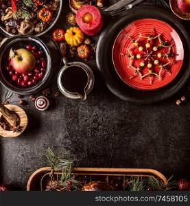 Christmas dinner background with festive table setting, snowflakes decoration, sauce, fresh cranberries and apple, pumpkins, nuts and pine branches. Dark rustic style. Top view. Copy space