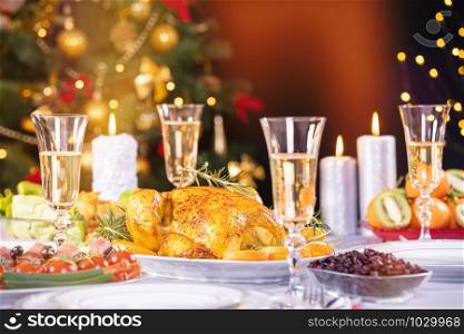 Christmas dinner. Chicken against glowing Christmas lights and burning candles. Holiday decorated table, Christmas tree, champagne and roasted turkey, Christmas served table. Focus on chicken!