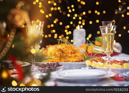 Christmas dinner. Closeup photo of tasty baked chicken against glowing Christmas lights and burning candles. Holiday decorated table, Christmas tree, champagne and roasted turkey, Christmas served table.