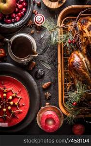 Christmas dinner. Festive table setting with roasted turkey served with pine branches and sauce on rustic background with burning candles, red plate, snowflakes decoration, fresh cranberries and apple