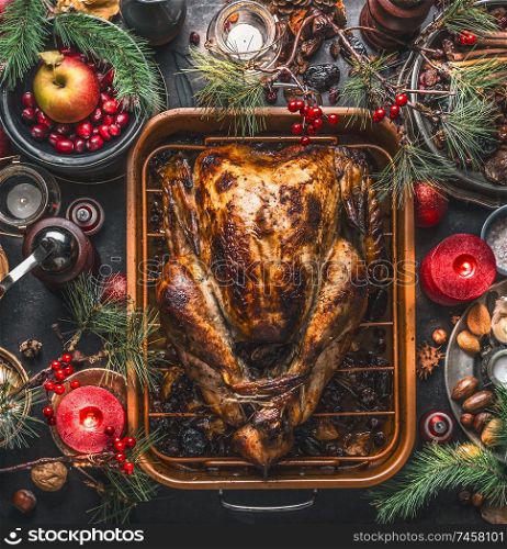 Christmas dinner. Roasted stuffed turkey served with fresh cranberries, pine branches on rustic background with burning candles, nuts, apple and little pumpkins, top view. Festive food flat lay