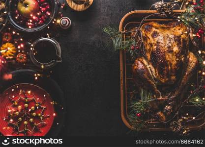 Christmas dinner table with whole roasted turkey, stuffed with dried fruits served with sauce,red plates, cutlery, decoration and burning candles, top view. Traditional Christmas food. Copy space