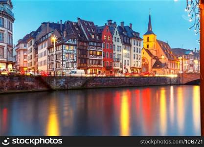 Christmas embankment in Strasbourg, Alsace. Picturesque Christmas quay and church of Saint Nicolas with mirror reflections in the river Ile during evening blue hour, Strasbourg, Alsace, France