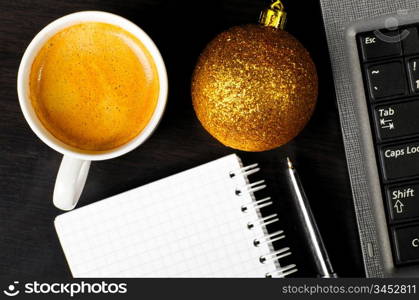 christmas eve at office, top view of coffee cup with golden ball, notepad and laptop