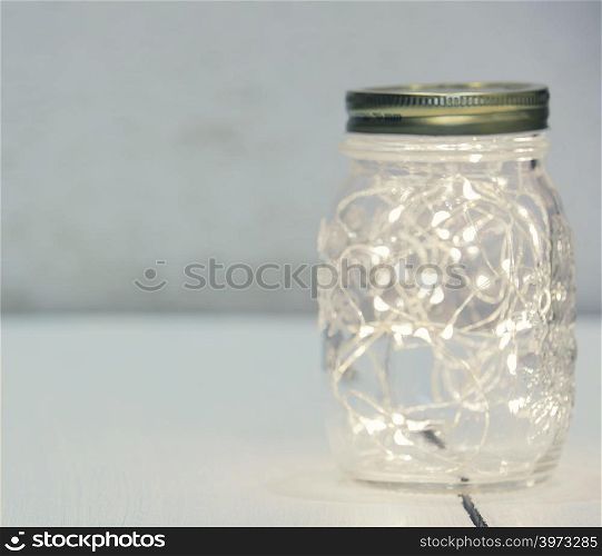 Christmas fairy lights in a mason jar glowing on rustic background.